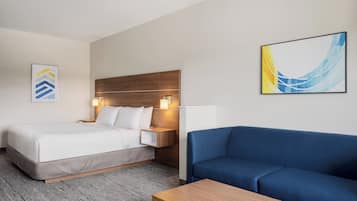 A hotel room with a bed, a blue sofa, a wooden coffee table, a nightstand with a lamp, and two wall-mounted artworks.