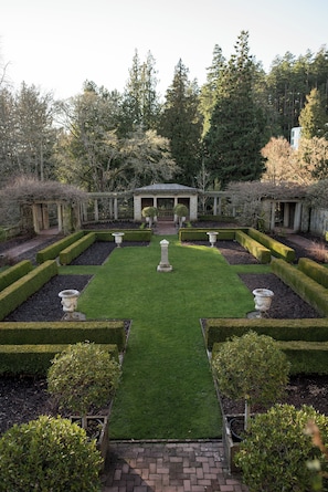A formal garden with a central lawn, symmetrical hedges, and a classical building structure.