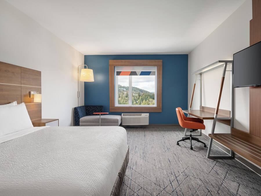 A hotel room with a bed, a desk, a chair, a TV, and a window with a view.