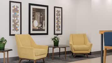 Un hall d’entrée avec deux fauteuils jaunes, une petite table sur laquelle est posée une plante, et des œuvres d’art encadrées accrochées au mur.