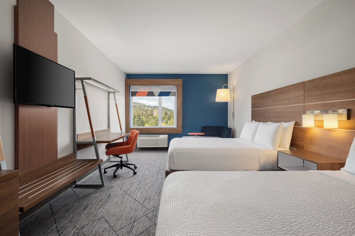 A hotel room with two beds, a desk, a chair, a TV, a window with a view, and a lamp.