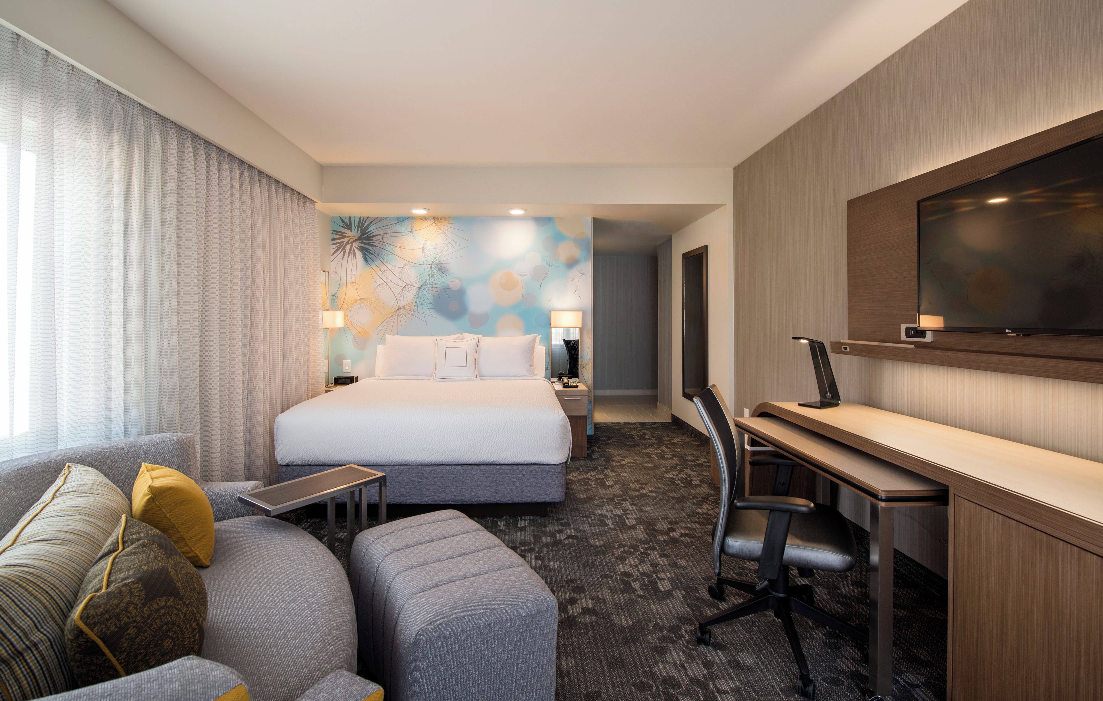 Une chambre d’hôtel avec un lit, un bureau, une chaise, une télévision et une fenêtre avec des rideaux.