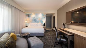 Une chambre d’hôtel avec un lit, un bureau, une chaise, une télévision et une fenêtre avec des rideaux.