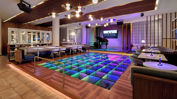 A modern lounge area with a wooden floor, seating arrangements, and a colorful LED dance floor. - Courtyard by Marriott Calgary South (Calgary)