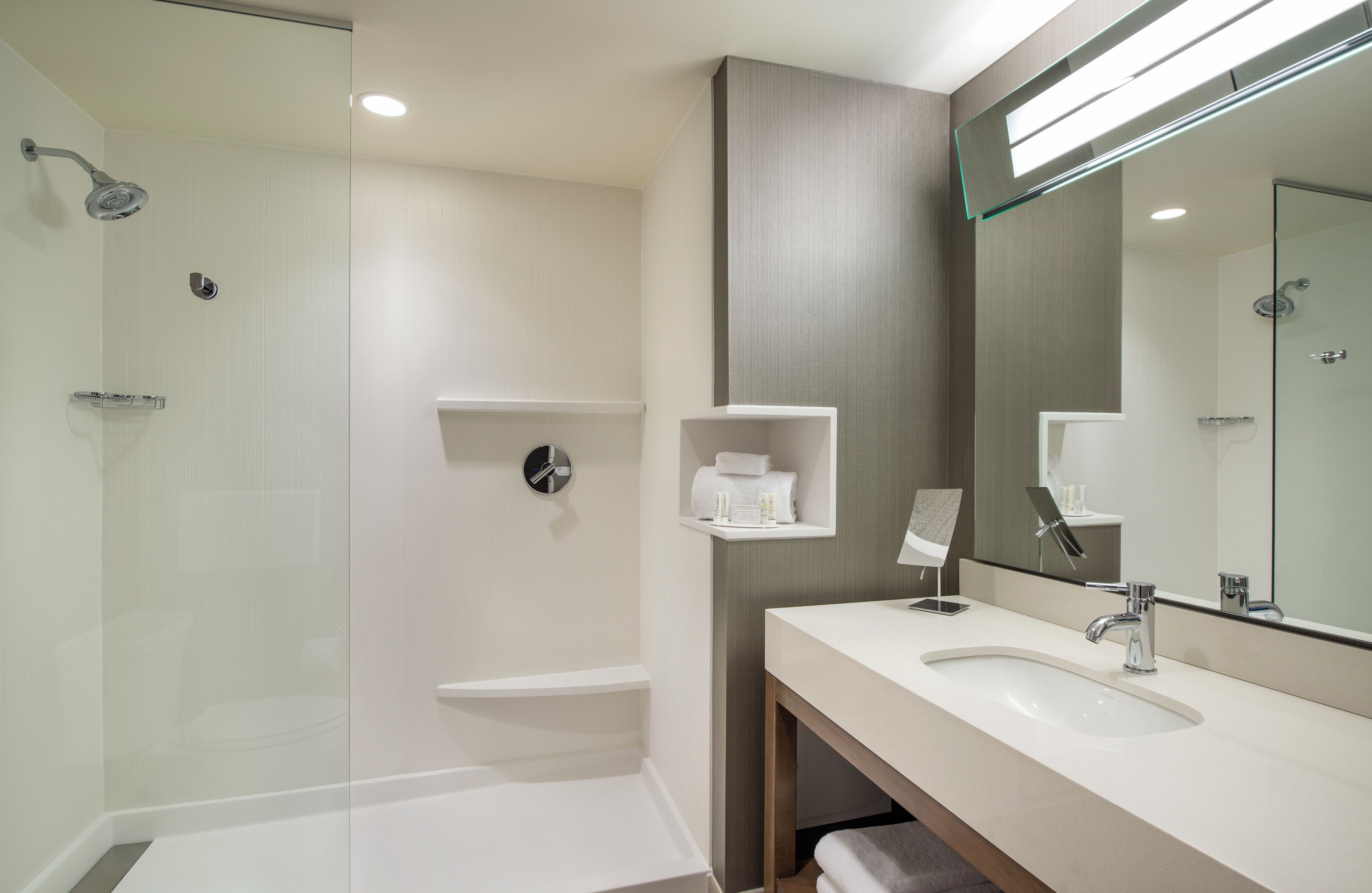 Un baño moderno con ducha de vidrio, tocador con espejo y toallero.