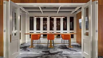 Un espace de salle à manger moderne avec une table en bois et des chaises orange, un plafond doté d’un éclairage encastré et un tapis à motifs.