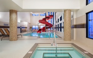 An indoor swimming pool with a red water slide, lounge chairs, and a no lifeguard on duty sign. - Courtyard by Marriott Calgary South (Calgary)