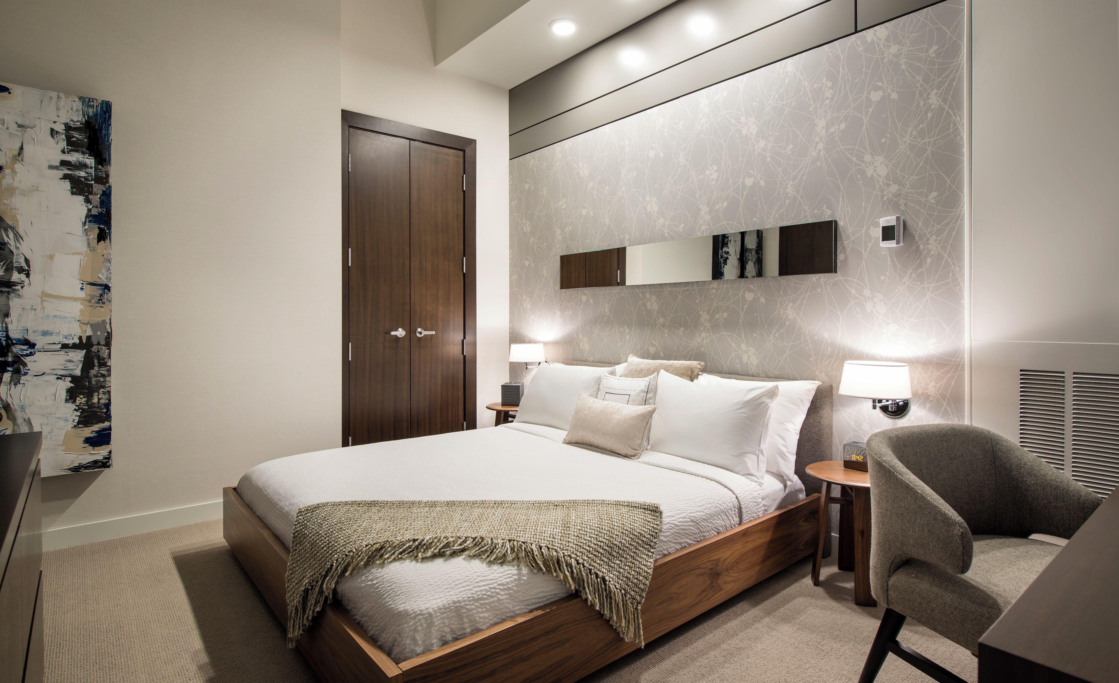 Une chambre moderne avec un grand lit, des lampes de chevet, un fauteuil et une armoire.