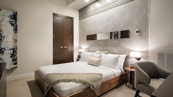 Une chambre moderne avec un grand lit, des lampes de chevet, un fauteuil et une armoire.