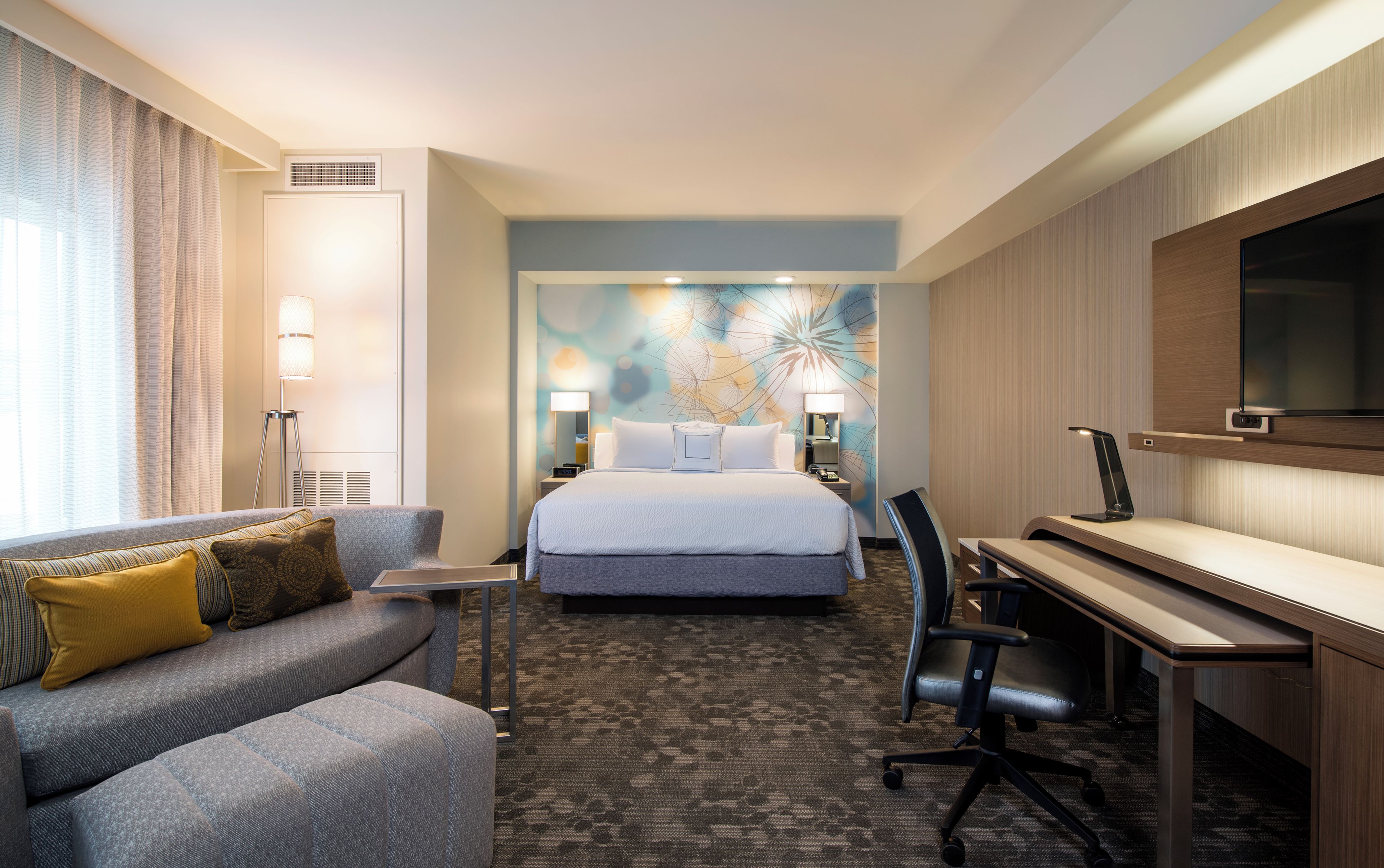 A hotel room with a bed, a desk, a sofa, and a TV.
