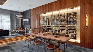 A modern interior with a wooden wall displaying a wine collection, a bar area with stools, and a seating area with a sofa and armchairs. - Courtyard by Marriott Calgary South (Calgary)