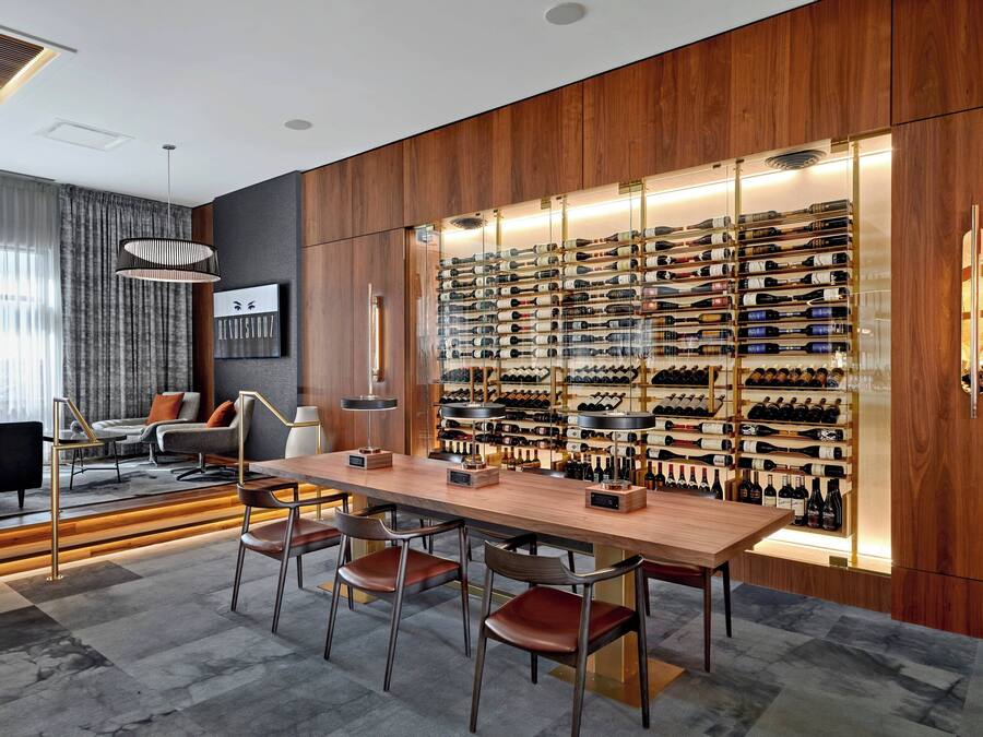 A modern interior with a wooden wall displaying a wine collection, a bar area with stools, and a seating area with a sofa and armchairs.