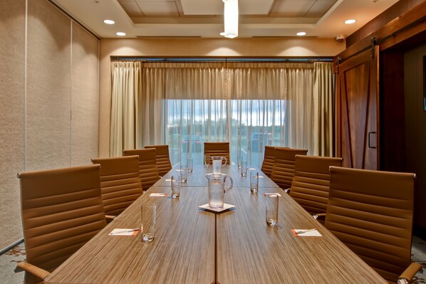 A conference room with a long table, brown chairs, and a large window with curtains.