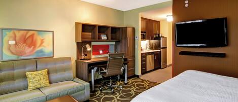 A hotel room with a bed, a sofa, a desk with a computer, a television, and a painting on the wall.