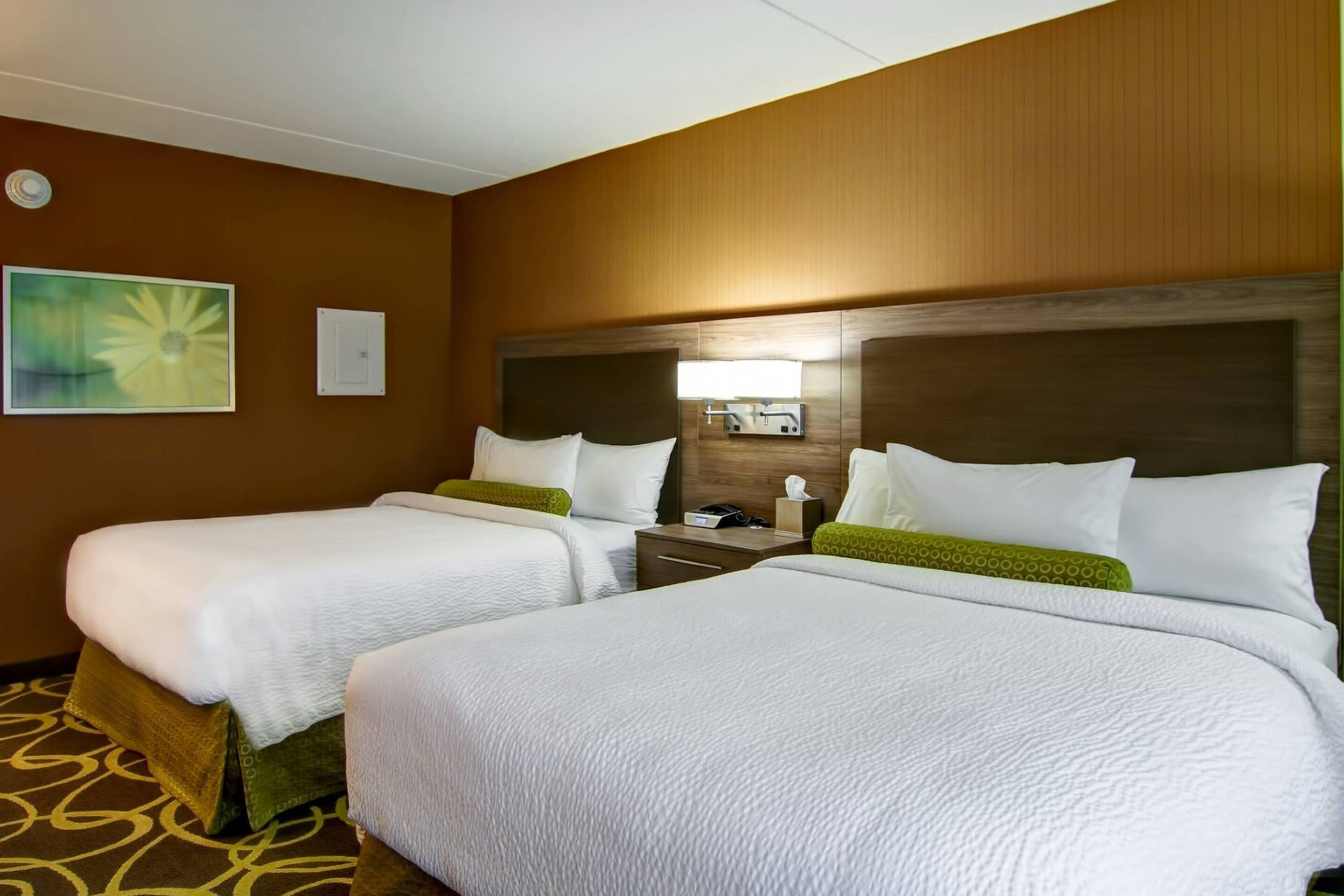 A hotel room with two beds, a nightstand, a lamp, and a painting on the wall.