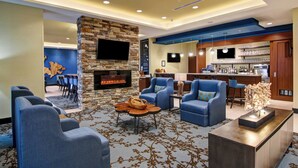 Een moderne hotel lobby met een stenen openhaard, blauwe zitplaatsen, een bar en een flatscreen televisie aan de muur.