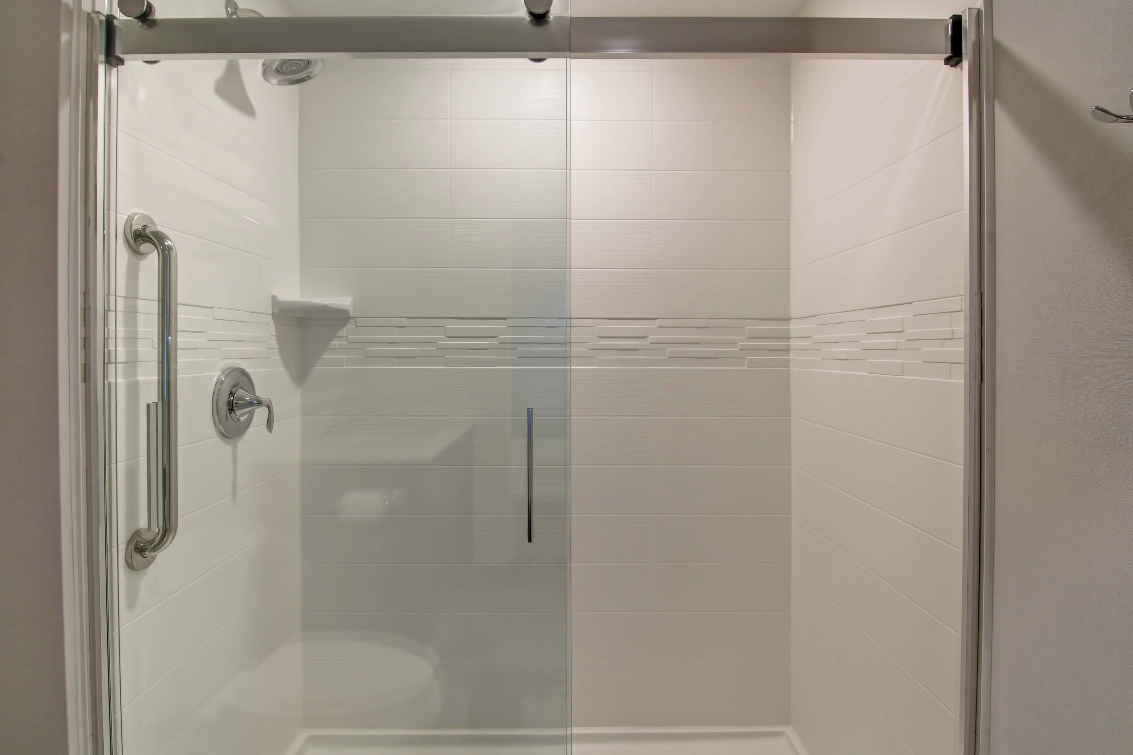 A glass-enclosed shower with white tiled walls and a clear glass door.