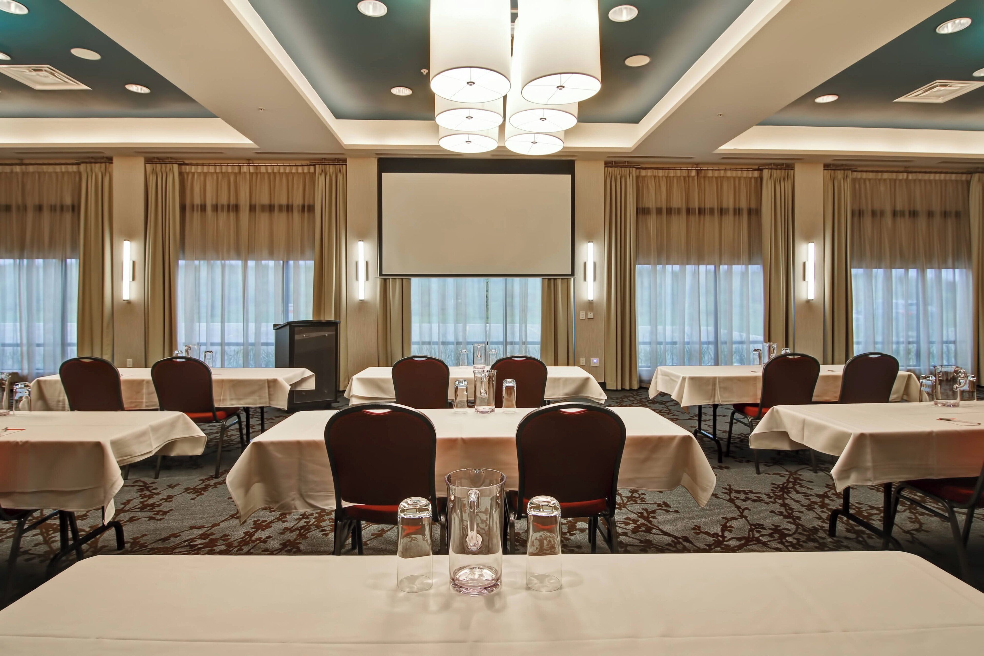 A conference room with tables, chairs, and a projector screen.