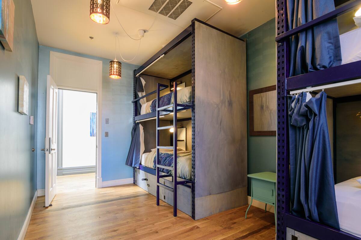 Una habitación con literas, una escalera, un escritorio y una puerta que da a otra habitación.