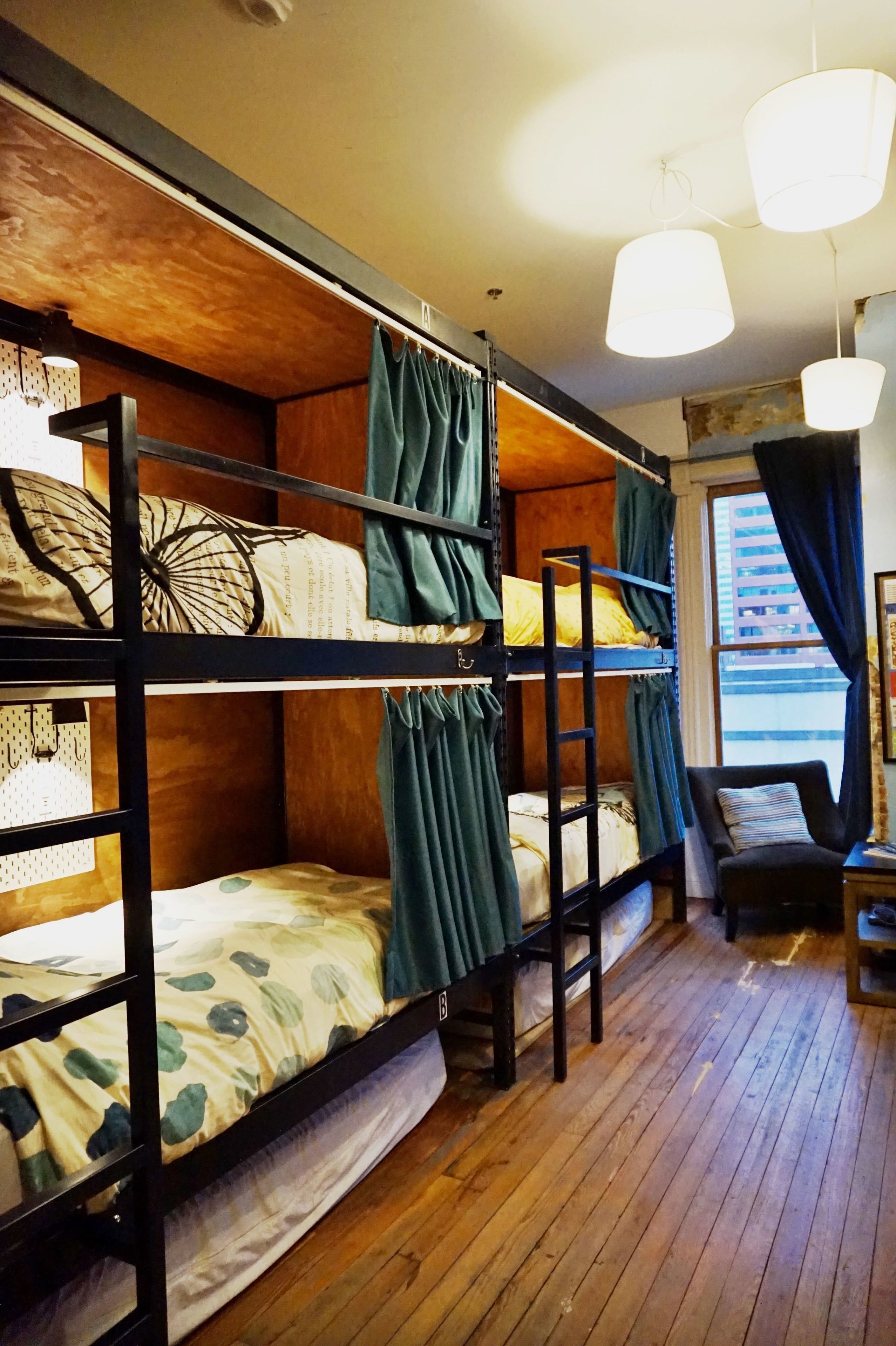 Une chambre avec un lit superposé, un plancher en bois, une chaise et une fenêtre avec des rideaux.