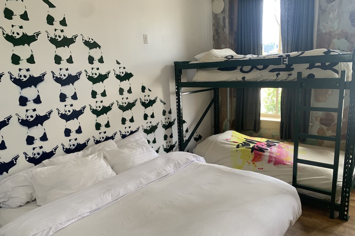 Una cama litera con ropa de cama blanca, una pared decorada con recortes de panda y una ventana con cortinas.