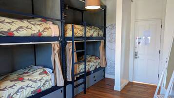 Habitación con literas, suelo de madera, una puerta blanca y una lámpara colgante.