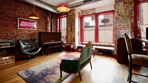 A room with a brick wall, a piano, a green armchair, a red hanging lamp, and a vintage Coca-Cola sign. - Hostel Fish (Denver)