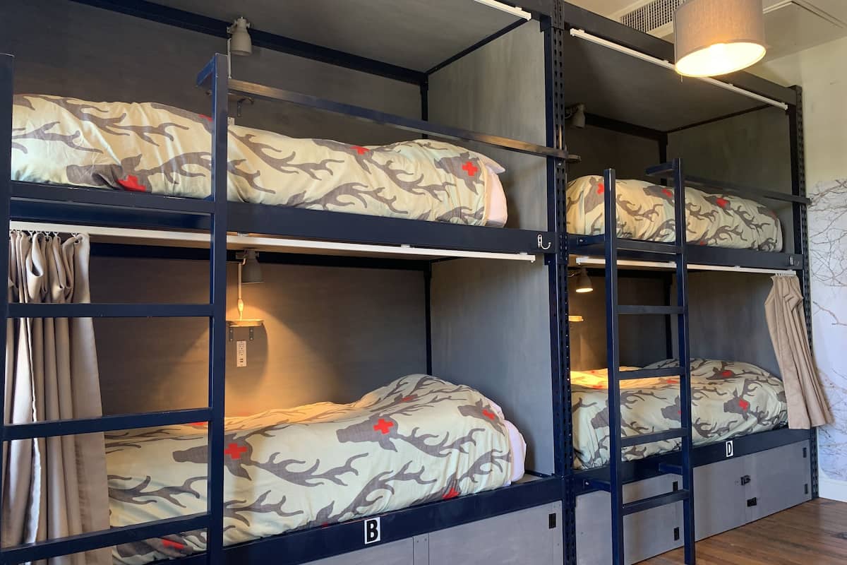 Habitación con literas escalonadas en tres niveles, cada una con ropa de cama de estampado camuflado y detalles rojos.
