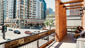 A balcony with a wooden railing overlooking a city street with tall buildings, a crosswalk, and parked cars. - Hostel Fish (Denver)