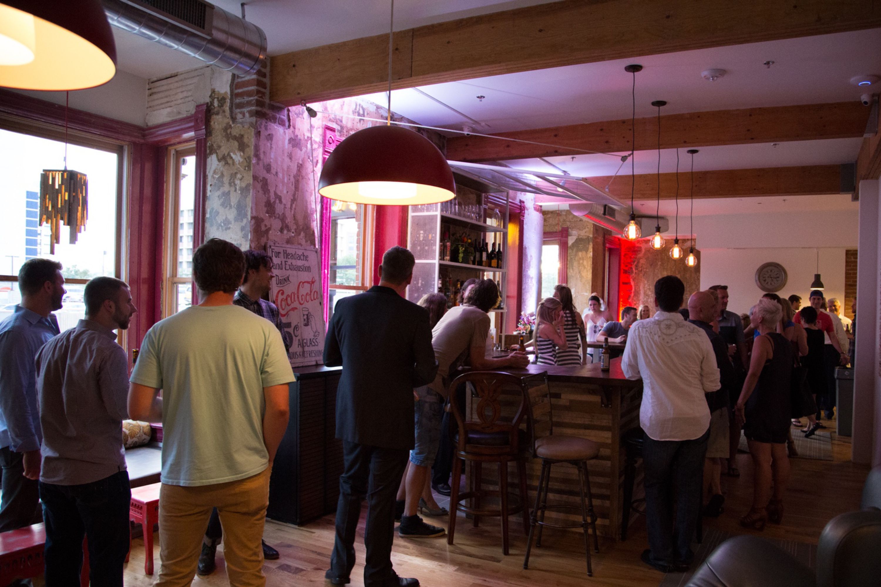 A crowded bar area with wooden beams, a large red pendant light, and a bar counter.