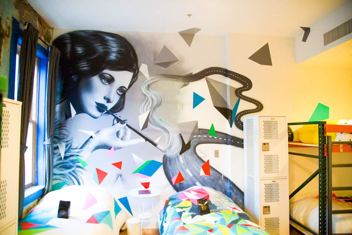 Una habitación con un mural de una mujer fumando, literas y decoraciones geométricas en la pared.