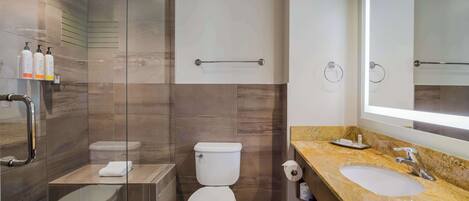 Un baño moderno con ducha envuelta en vidrio, inodoro, lavabo y un espejo grande.