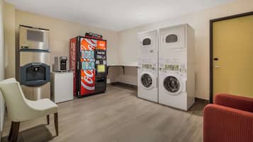 A hotel room with a sofa, a vending machine, a coffee machine, and a washing machine.