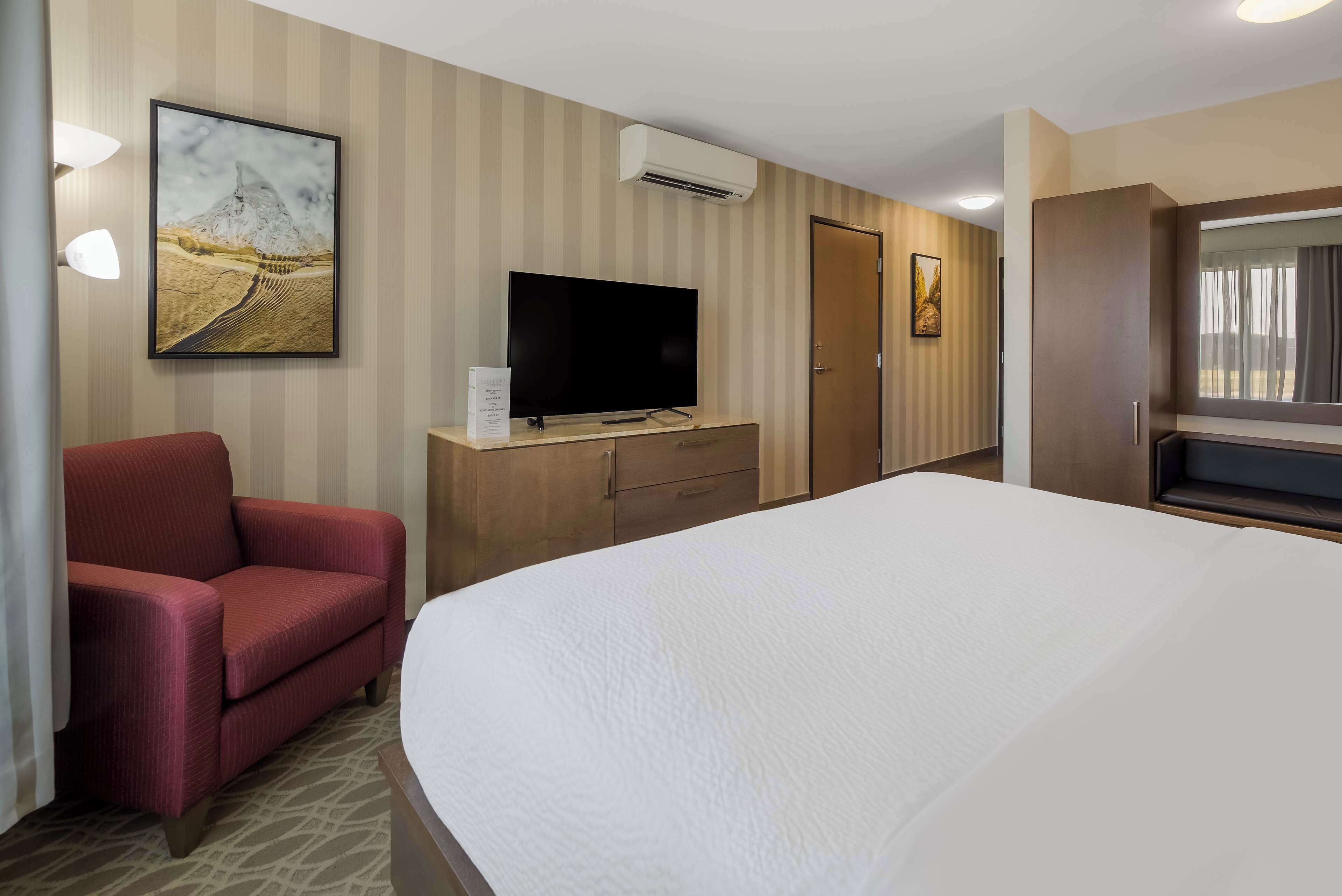 A hotel room with a large bed, a TV on a wooden cabinet, a red armchair, and a painting on the wall.