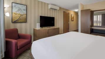 A hotel room with a large bed, a TV on a wooden cabinet, a red armchair, and a painting on the wall.