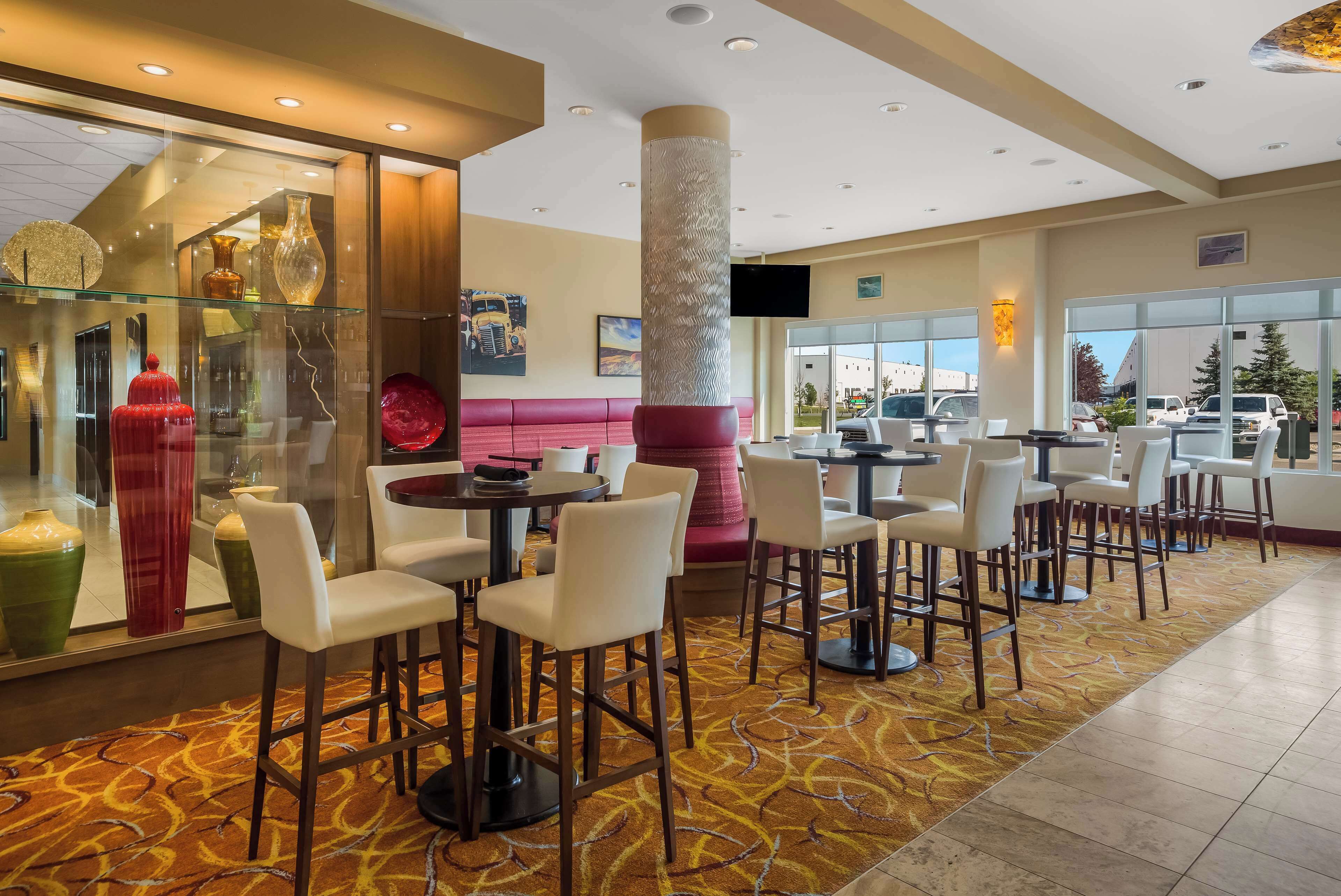 A modern hotel lobby with a glass display of decorative vases, a central seating area with a red bench, and a large pillar.
