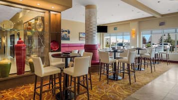A modern hotel lobby with a glass display of decorative vases, a central seating area with a red bench, and a large pillar.