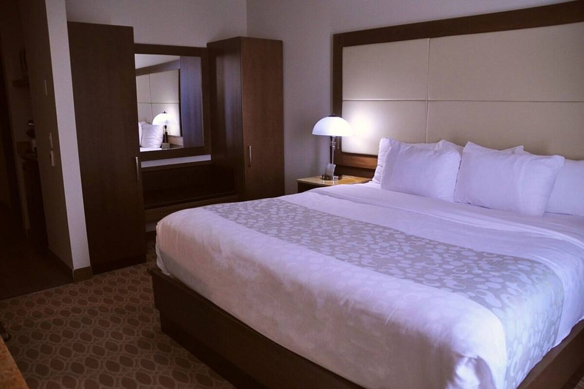 Una habitación de hotel con una cama grande, una mesita de noche con lámpara, un armario y un espejo.