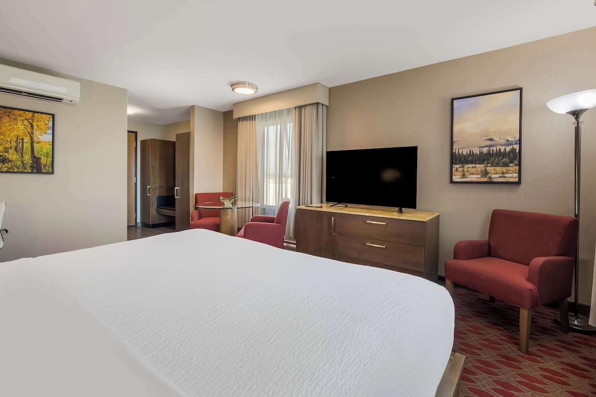 Una habitación de hotel con una cama grande, un escritorio, un televisor, un sillón rojo y un cuadro en la pared.