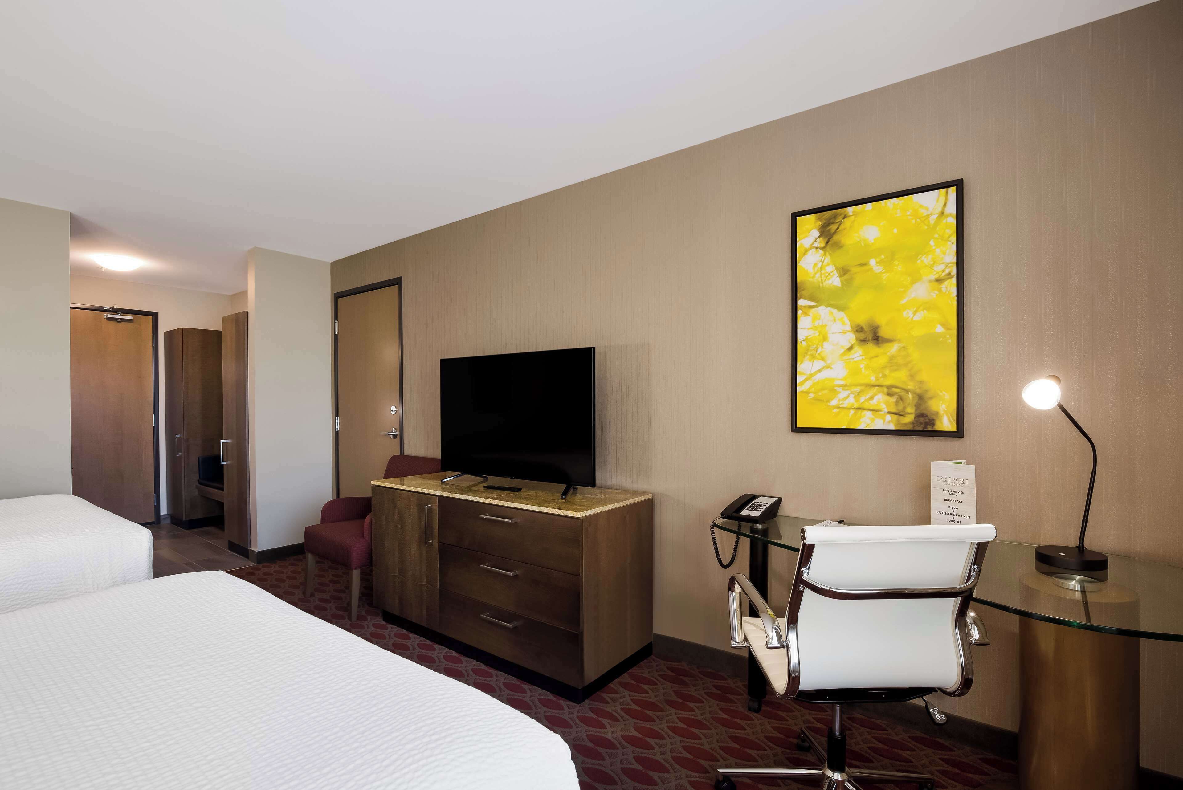 A hotel room with a bed, a TV, a desk with a chair, and a telephone.