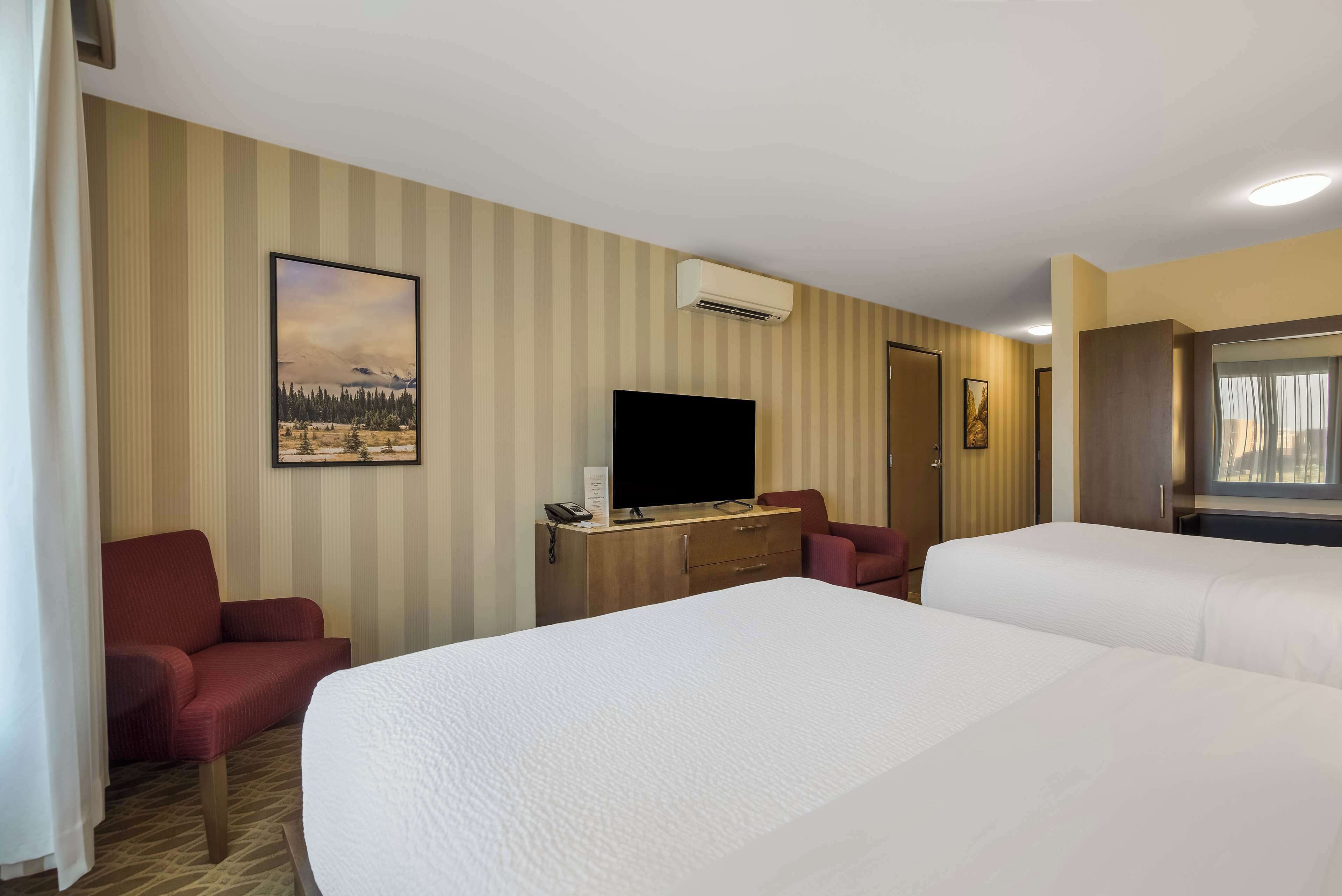 Habitación de hotel con dos camas, televisión, escritorio con teléfono y un cuadro en la pared.