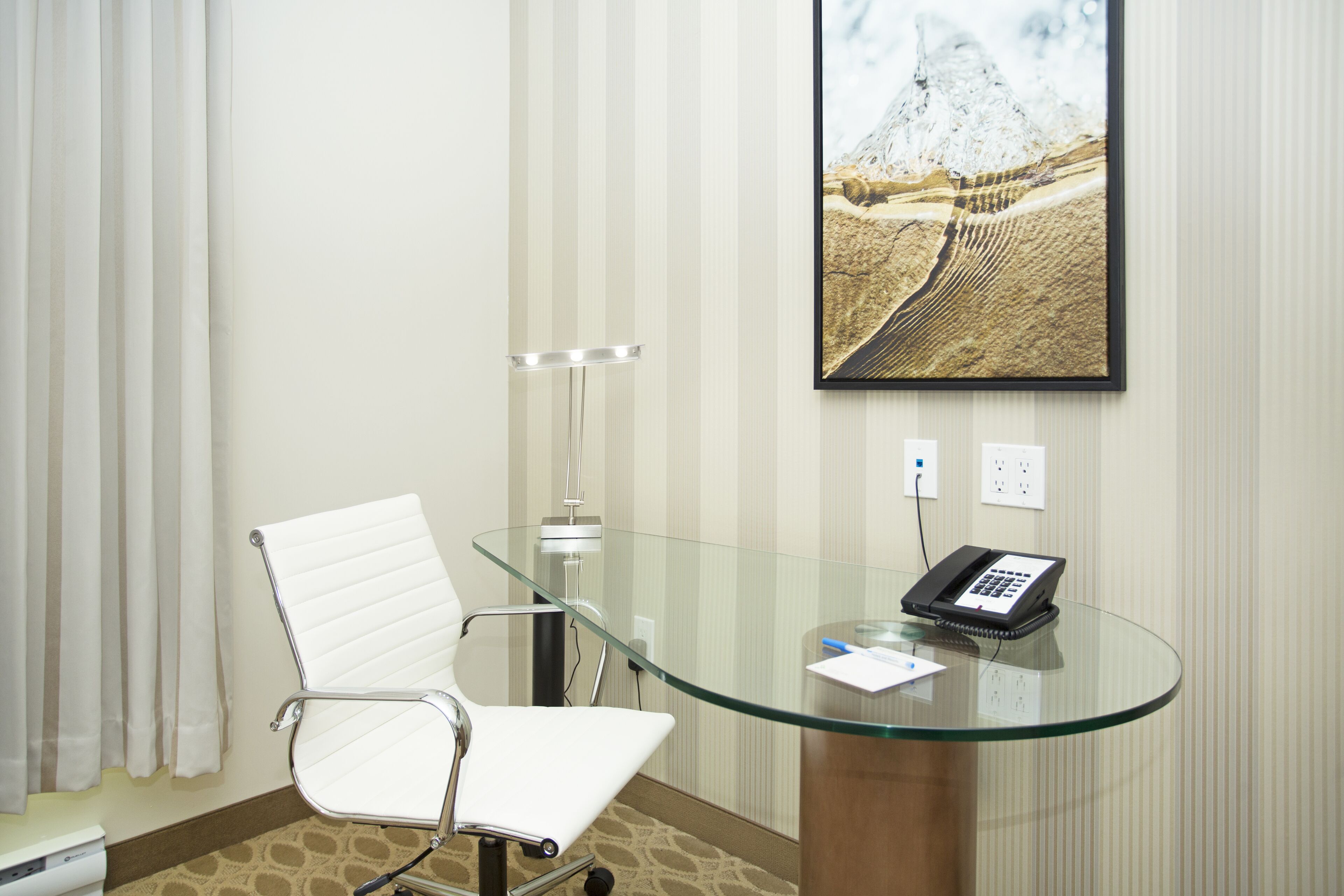 Une salle de conférence avec une table en verre, une chaise blanche, un téléphone et un tableau représentant une montagne.