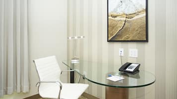 Une salle de conférence avec une table en verre, une chaise blanche, un téléphone et un tableau représentant une montagne.