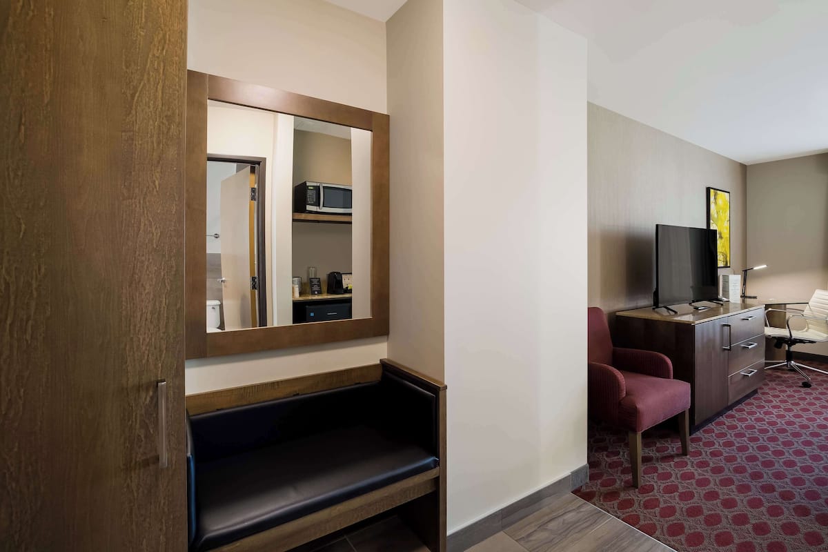 Habitación de hotel con un banco de madera, televisión, escritorio y alfombra roja estampada.