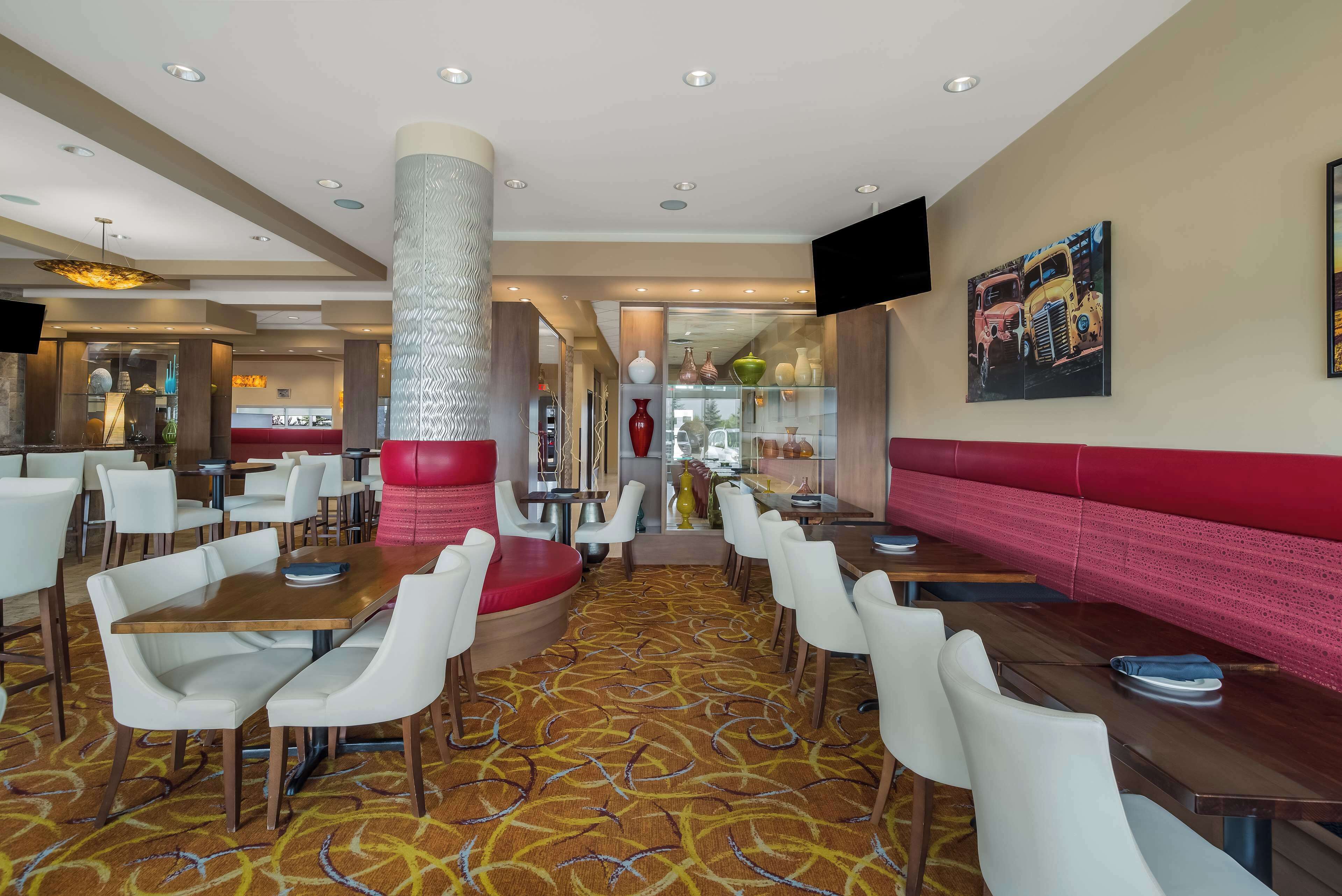 Un hall d’hôtel doté de plusieurs espaces aménagés avec des sièges, notamment des tables et des banquettes, un tapis à motifs et une grande colonne.