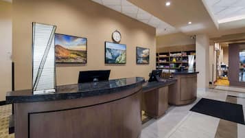 A reception desk with a clock, three framed landscape paintings, and a staircase leading to the upper floor.
