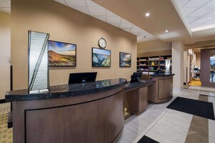 A reception desk with a clock, three framed landscape paintings, and a staircase leading to the upper floor.