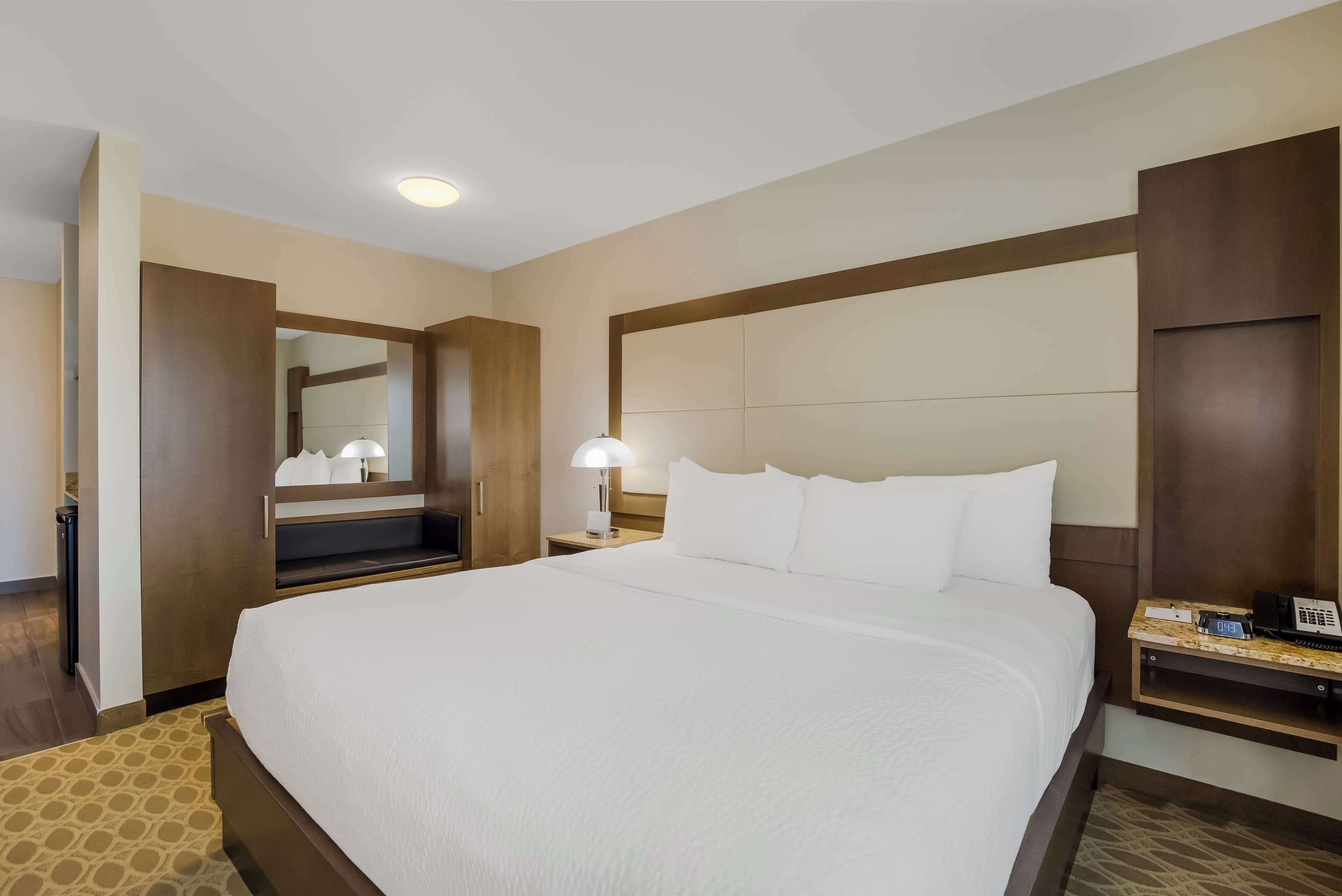 Una habitación de hotel con una cama grande, una mesita de noche con lámpara, un espejo y un teléfono.