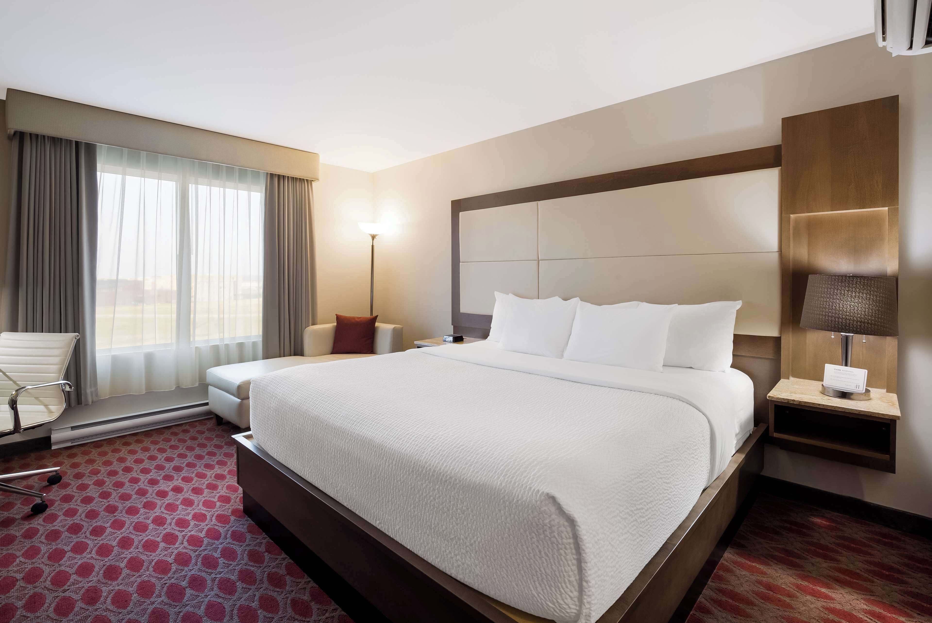 A hotel room with a large bed, a chair, a nightstand, and a lamp.