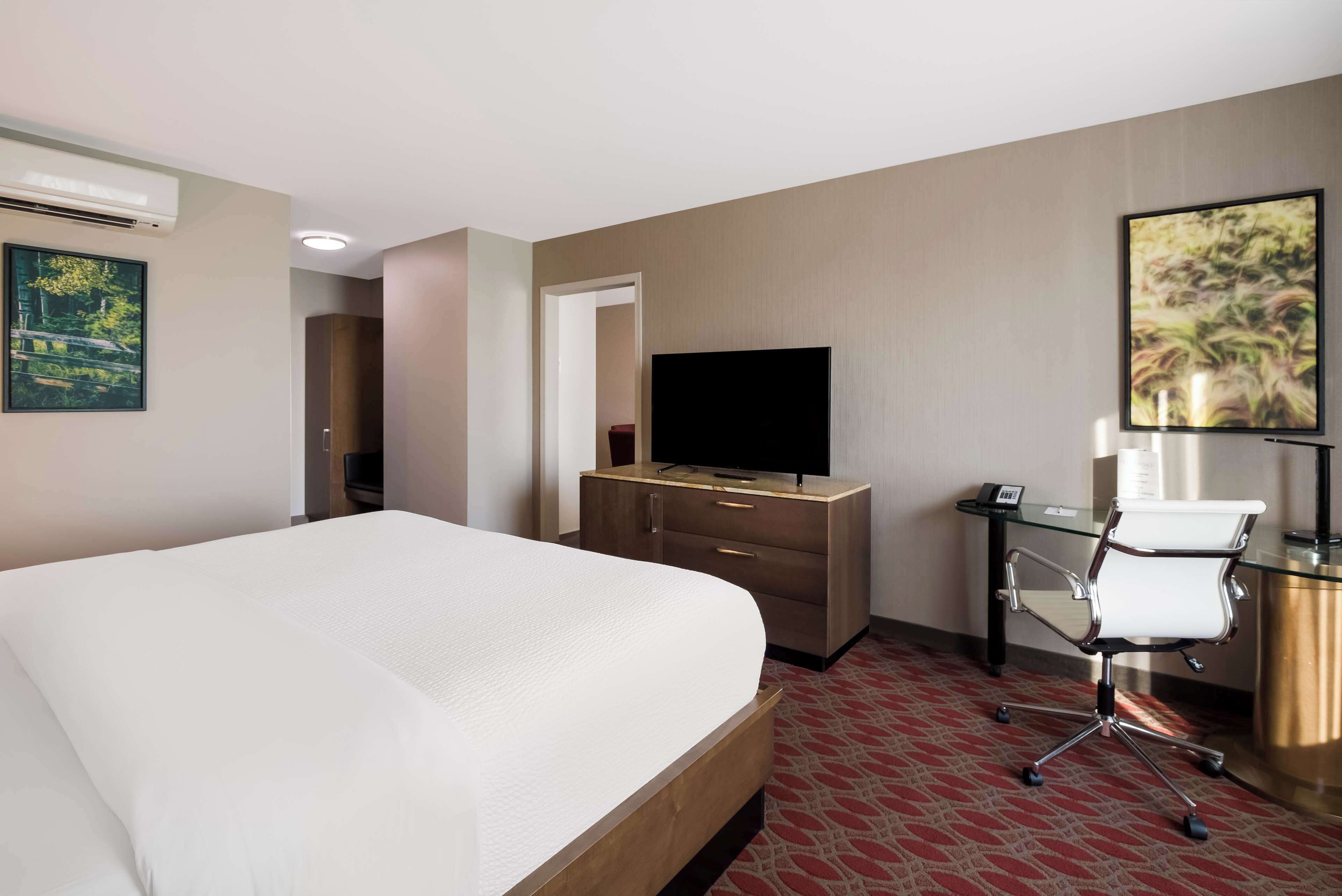 A hotel room with a large bed, a desk with a chair, a television, and a painting on the wall.